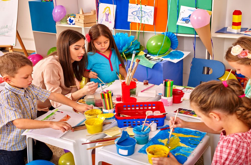 children with woman teacher painting on paper in kindergarten
