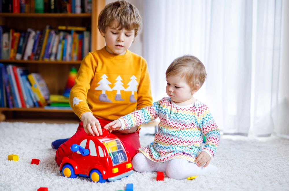 happy white baby girl and white toddler boy playing with different colorful toys