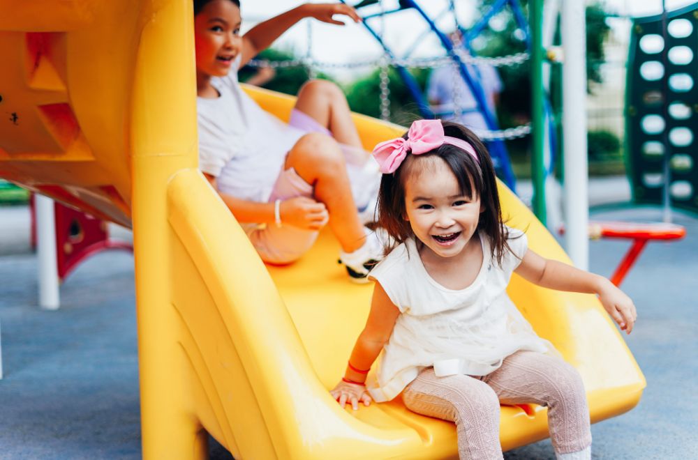 Asian toddler playing on yellow slide