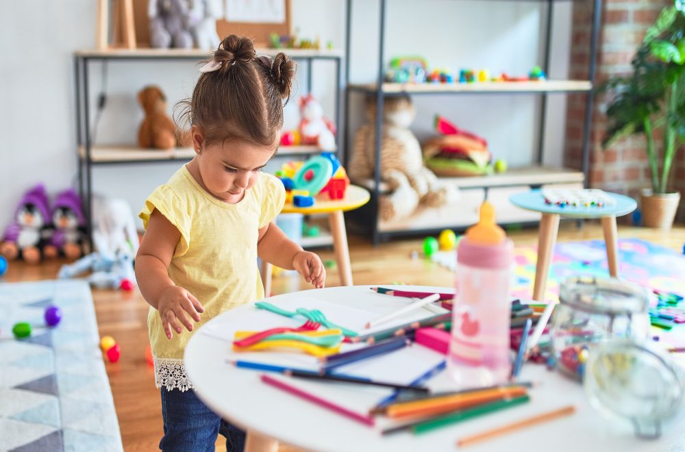 Hispanic toddler standing toddler girl holding colored pencils at preschool