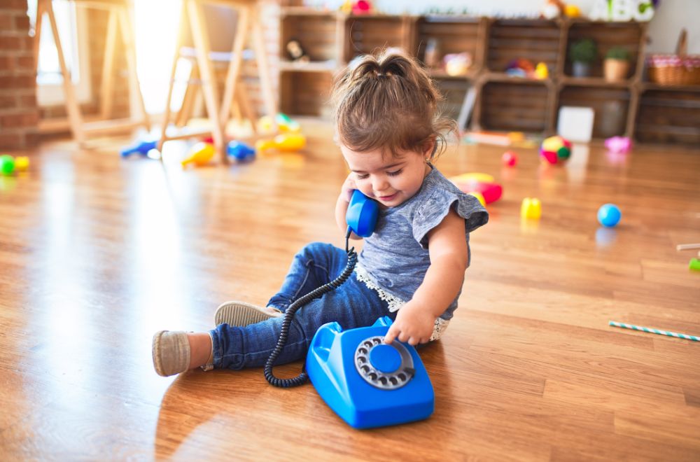 toddler girl sitting on the floor playing with vintage phone at kindergarten
